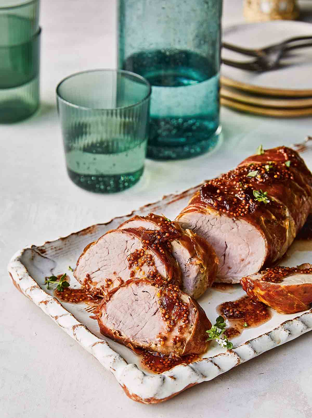 En skivad airfryer prosciutto-lindad fläskfilé täckt av senaps-fikonsås på ett vitt fat