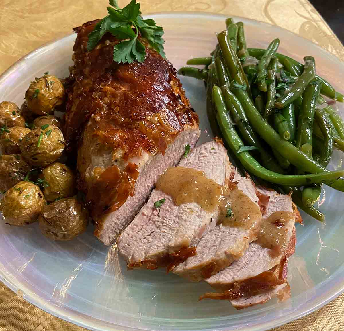 A sliced air fryer prosciutto-wrapped pork tenderloin on a plate with green beans and roasted baby potatoes