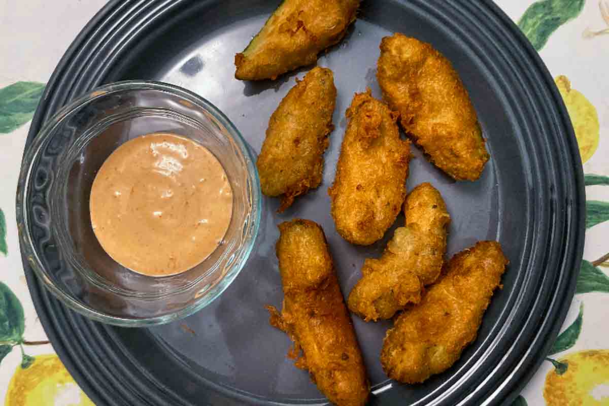 Seven beer-battered avocado dippers on a grey plate with a small dish of chipotle mayo beside them