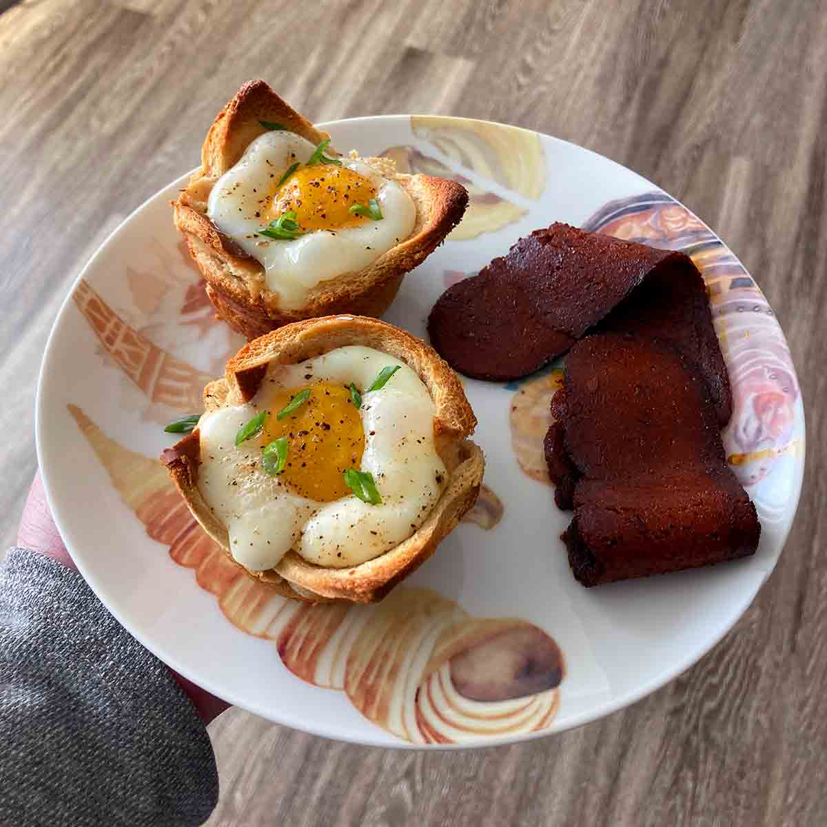 Two baked egg and toast cups on a plate with a strip of bacon