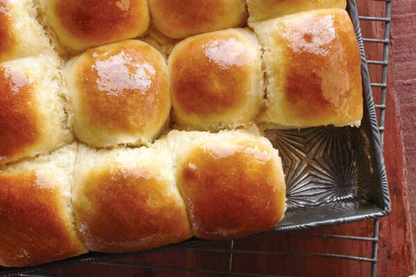 Tray of classic dinner rolls glazed with butter, bowl of melted butter with a brush