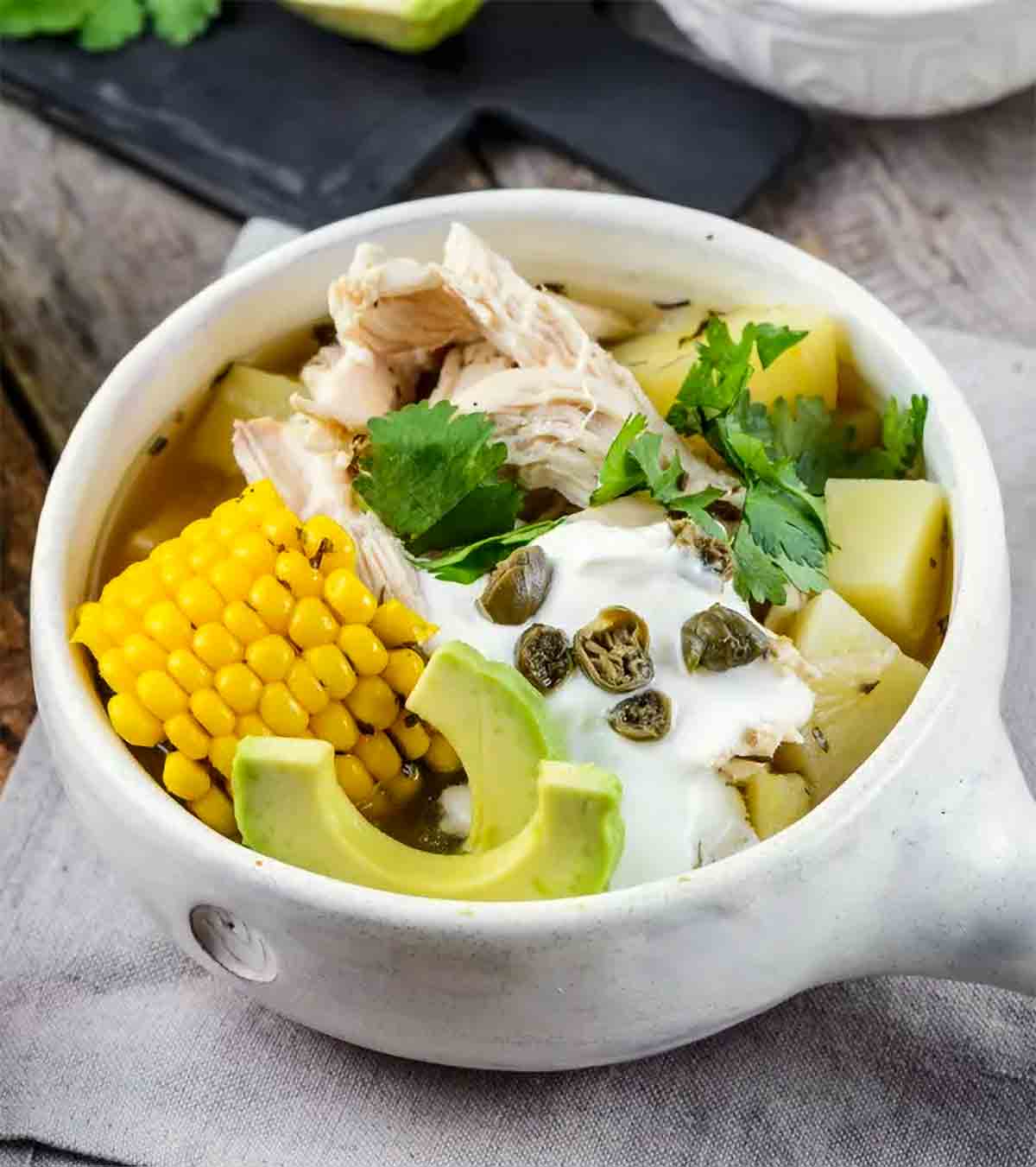 A white bowl filled with Colombian chicken and potato stew with corn and avocados