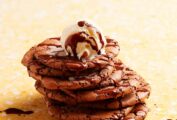 A stack of cracked brownie cookies with chocolate sauce and ice cream on top