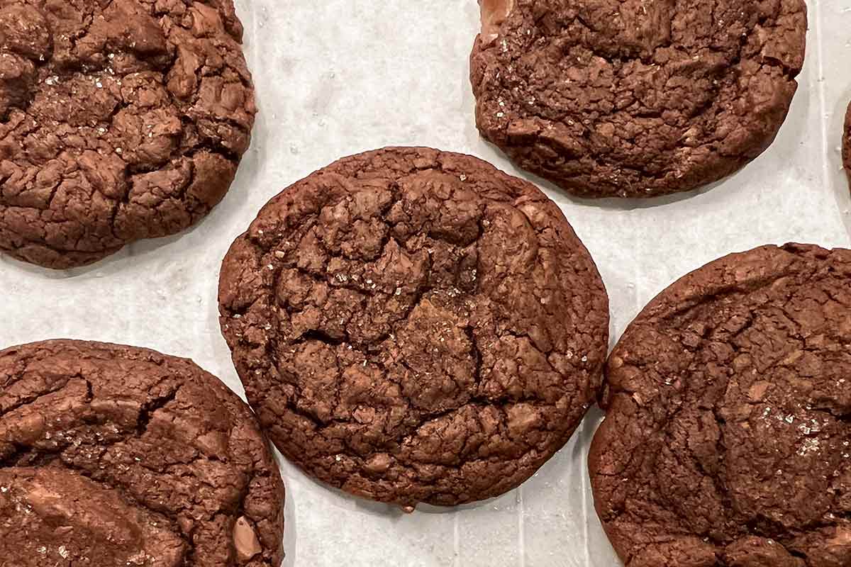Several cracked brownie cookies on a piece of parchment paper