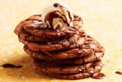 A stack of cracked brownie cookies with chocolate sauce and ice cream on top