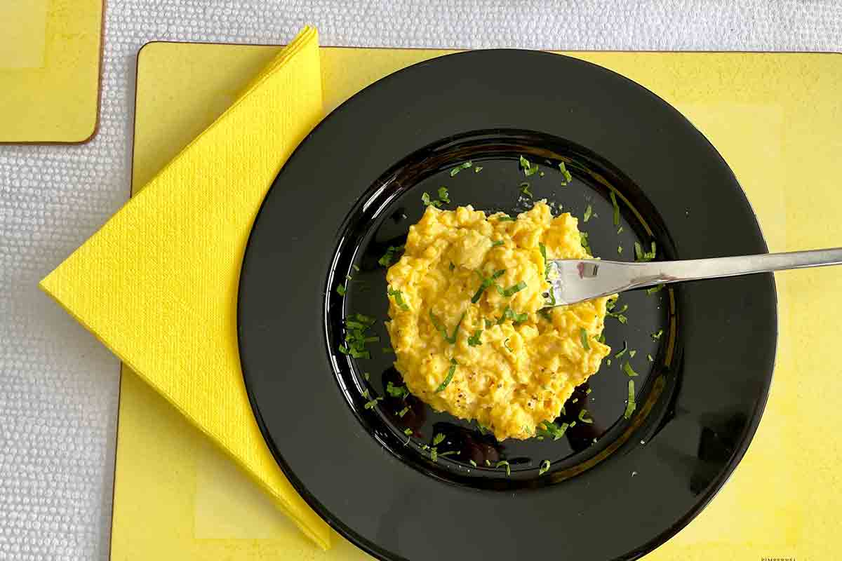 A black plate topped with easy scrambled eggs on a yellow placemat with a yellow napkin on the side