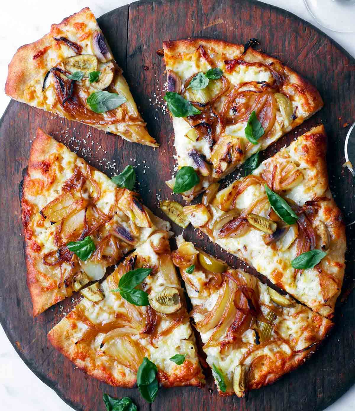 A fennel and sweet onion pizza with green olives on a wooden cutting board