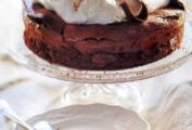 A flourless chocolate cloud cake on a glass cake stand on a white tablecloth