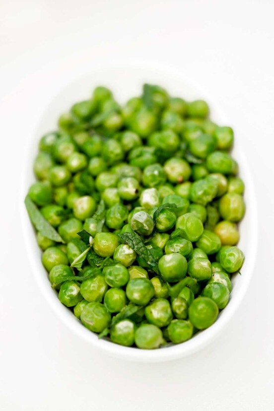 White bowl of fresh peas with mint.
