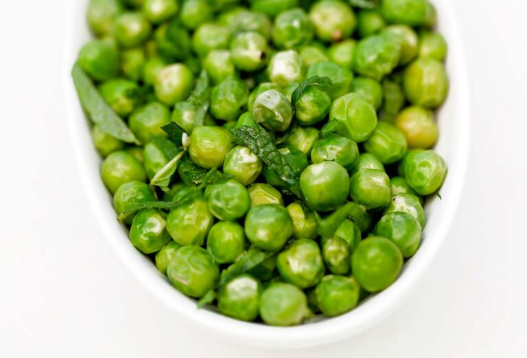 White bowl of fresh peas with mint.