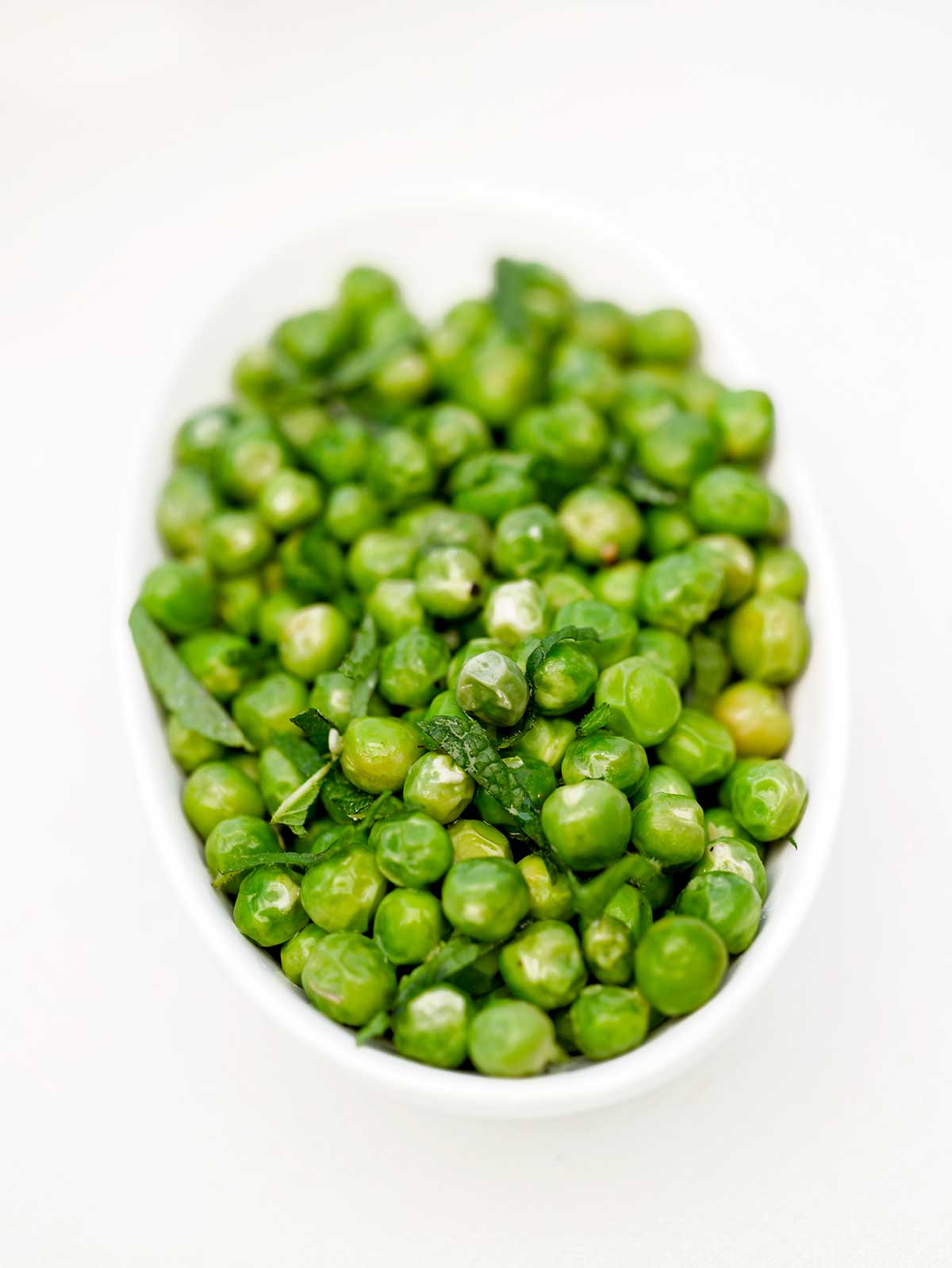 White bowl of fresh peas with mint.