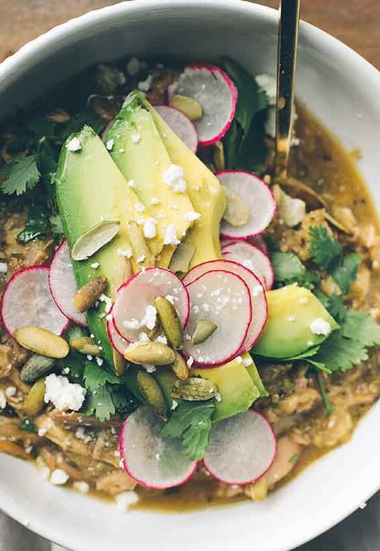 A white bowl filled with pozole verde, topped with sliced radishes, pepitas, avocado, and cilantro.