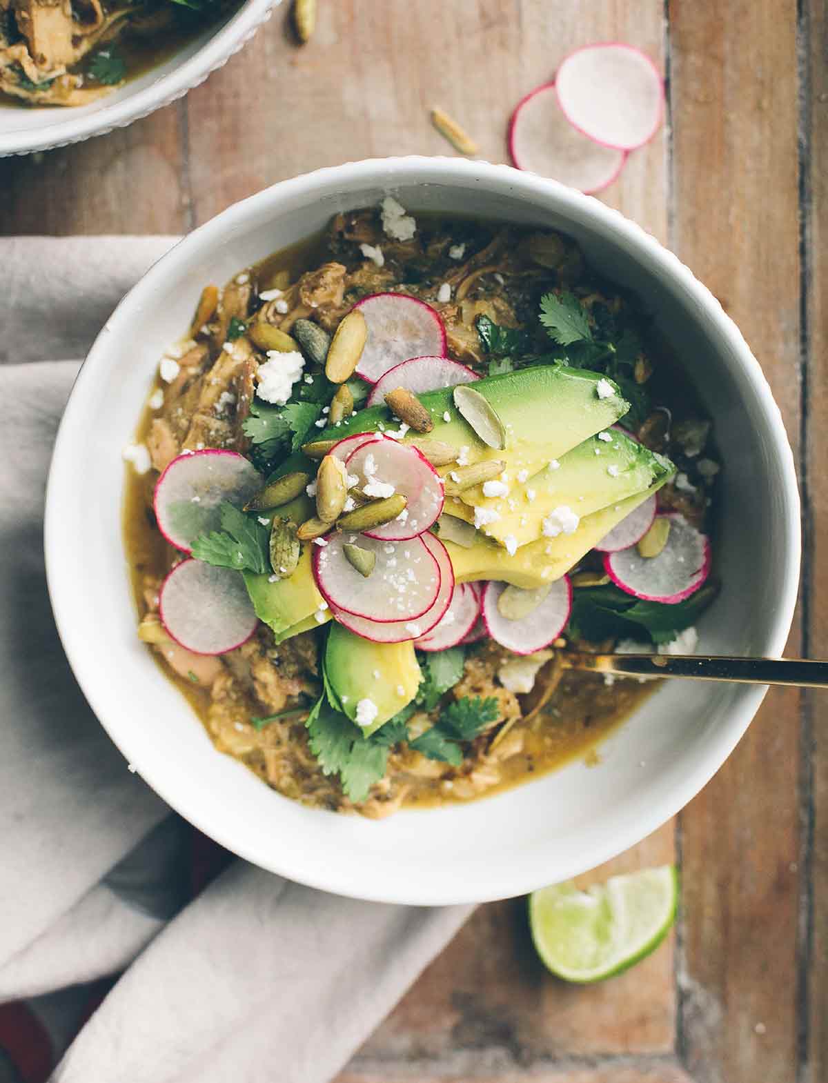 A white bowl filled with pozole verde, topped with sliced radishes, pepitas, avocado, and cilantro.