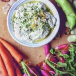 Herbed ricotta dip with a cutting board covered with carrots, radishes, fava beans