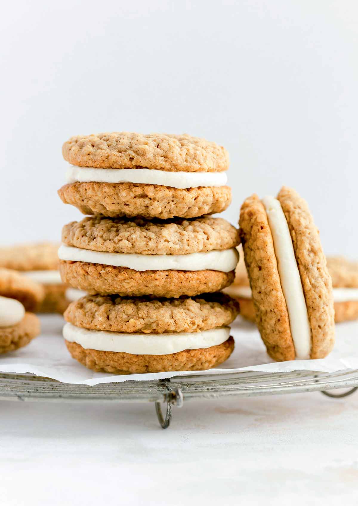 A stack of homemade oatmeal cream pies on a sheet of parchment with a few more scattered around