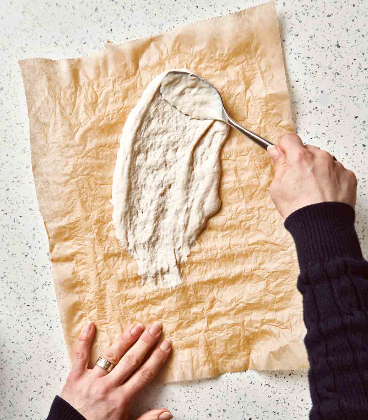 A person spreading sourdough starter on a sheet of parchment