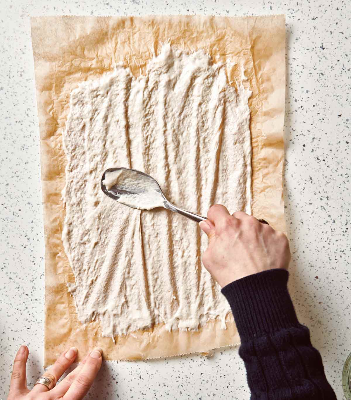 A person spreading sourdough starter on a piece of parchment