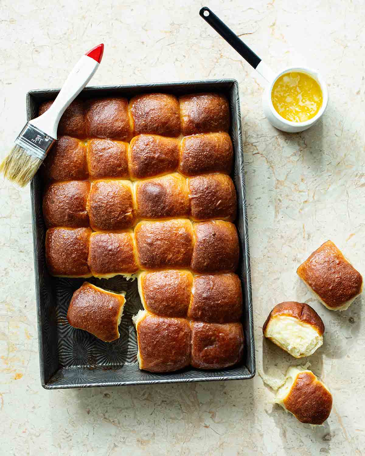 A rectangular pan of Cheryl Day's icebox rolls with a pastry brush resting on the side and a small dish of butter