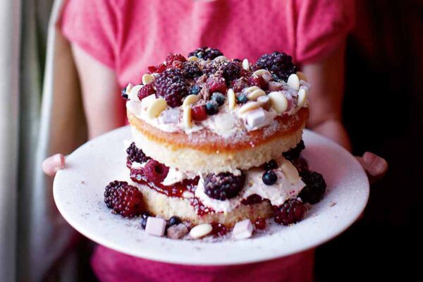 Young girl holding an two-layer iced berry cake filled with raspberries, blueberries, strawberries, and whipped cream