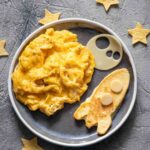A round plate filled with easy scrambled eggs and a pancake in the shape of a rocket with pastry stars scattered around it