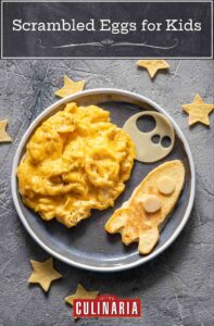 A round plate filled with easy scrambled eggs and a pancake in the shape of a rocket with pastry stars scattered around it