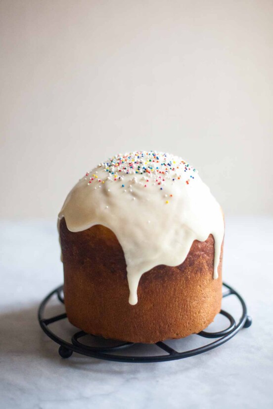 A loaf of kulich topped with glaze and sprinkles on a round trivet