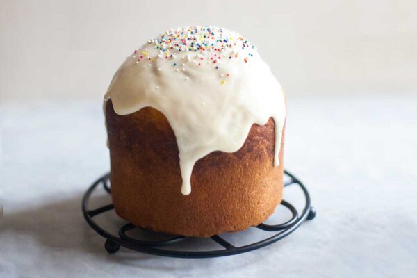 A loaf of kulich topped with glaze and sprinkles on a round trivet