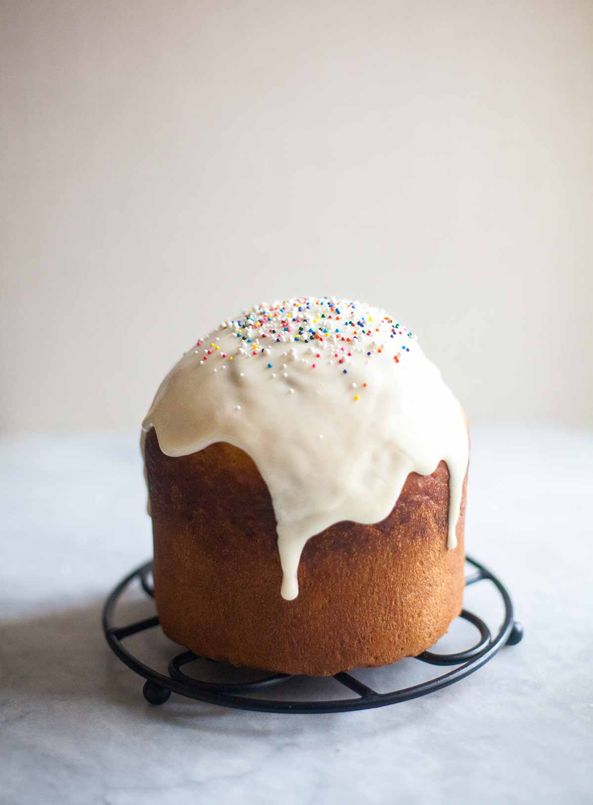 A loaf of kulich topped with glaze and sprinkles on a round trivet