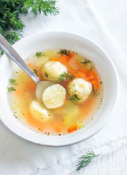 A white bowl filled with matzo ball soup and sprinkled with dill