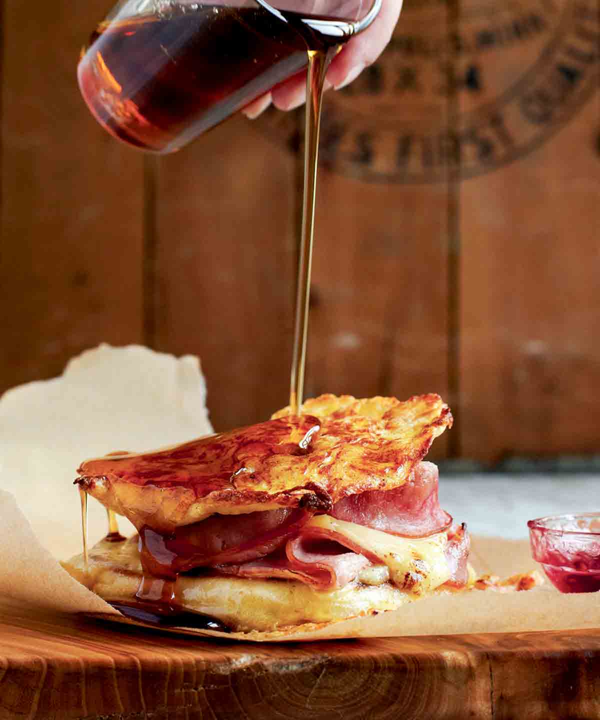 Maple syrup being poured over a monte cristo sandwich that is on a piece of parchment paper.
