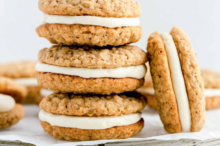 A stack of homemade oatmeal cream pies on a sheet of parchment with a few more scattered around