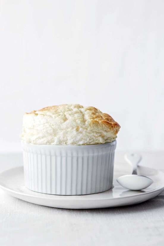 Ramekin with a parmesan souffle on a white plate, spoon, white tablecloth
