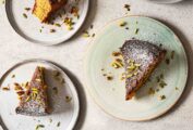 Several plates with slices of pistachio-lime polenta cake topped with confectioners' sugar and chopped pistachios