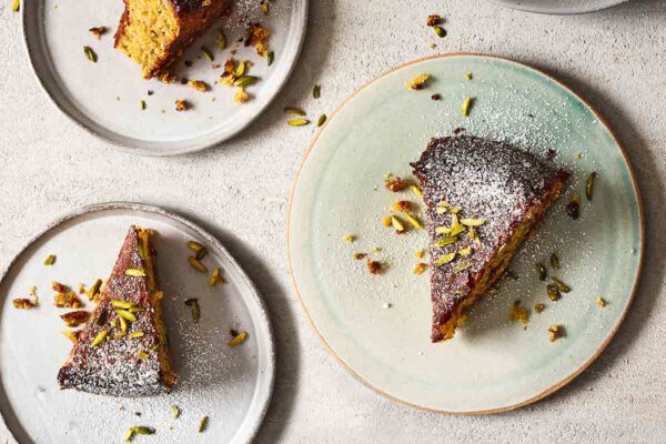 Several plates with slices of pistachio-lime polenta cake topped with confectioners' sugar and chopped pistachios