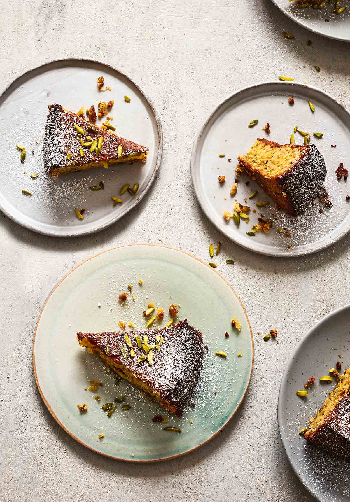 Several plates with slices of pistachio-lime polenta cake topped with confectioners' sugar and chopped pistachios