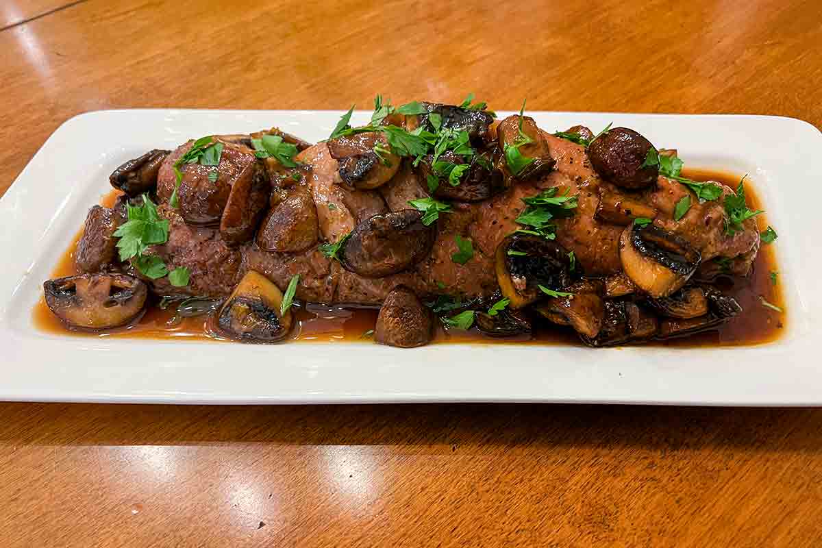 A piece of pork topped with mushrooms and sauce on a rectangular serving platter