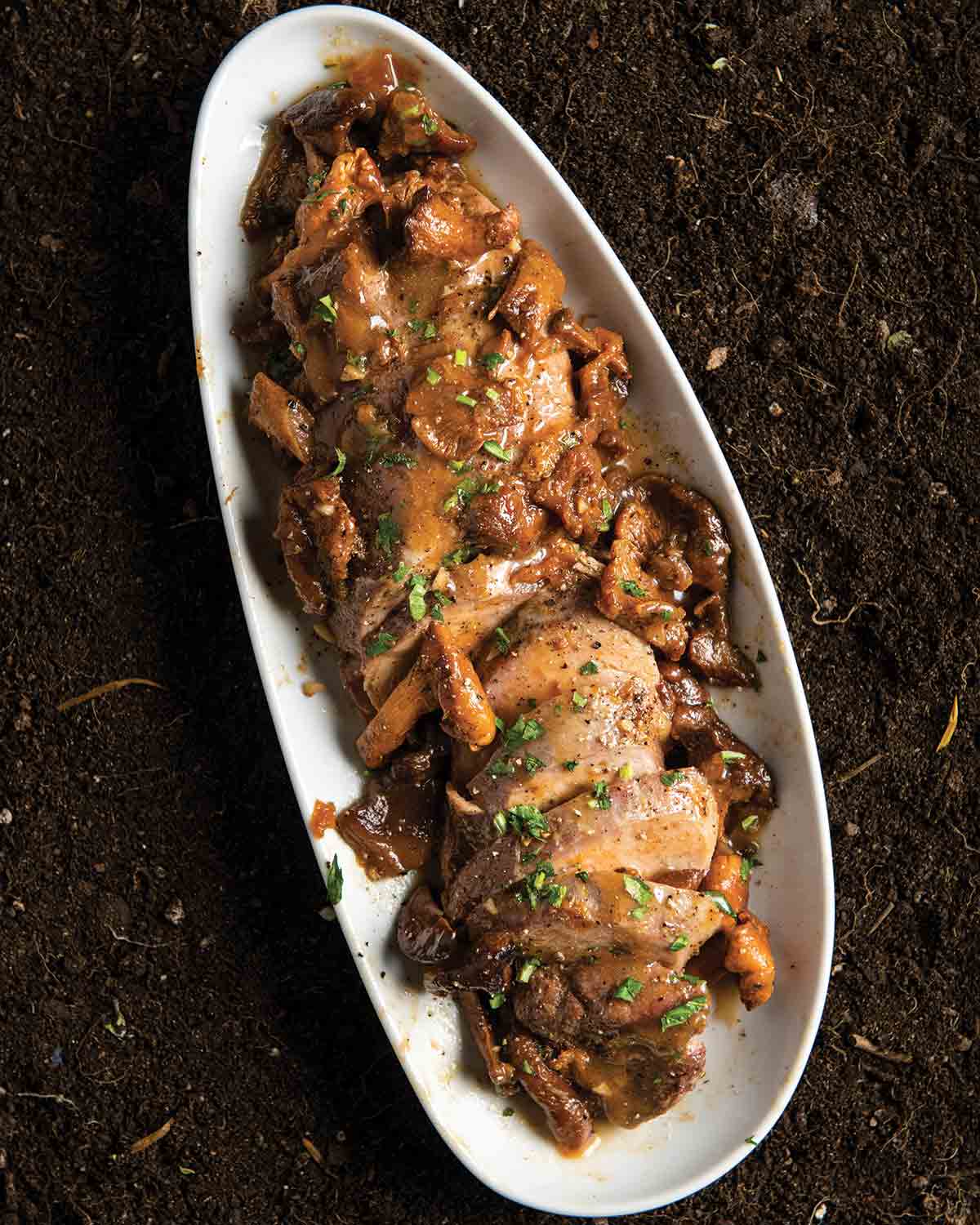 An oval platter containing sliced pork with chanterelles and apricot jam sauce