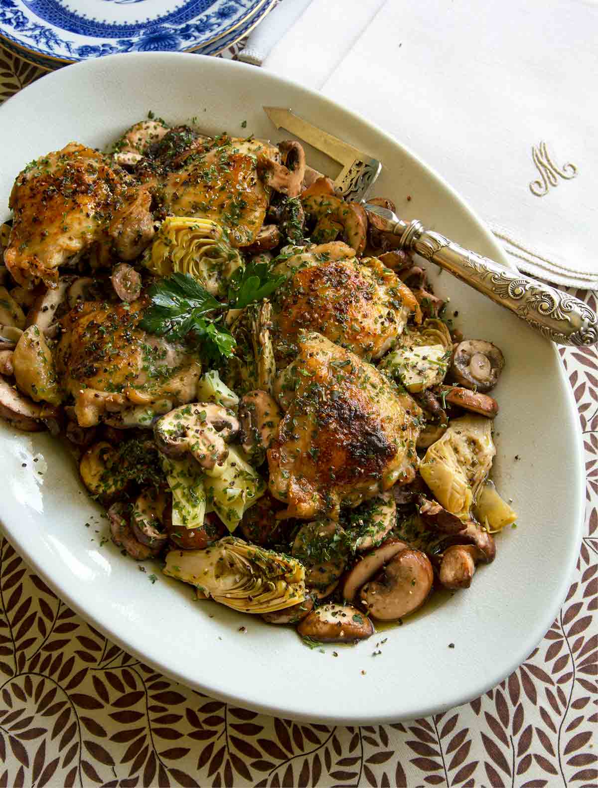 A white oval platter topped with sherry-braised chicken with artichoke hearts