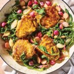 A white enameled skillet filled with chicken thighs, halved radishes, and radish greens