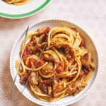 En rund pastaskål fylld med rökig pulled chicken bucatini med serveringstång vilande på skålen