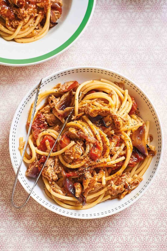 A round pasta bowl filled with smoky pulled chicken bucatini with serving tongs resting on the bowl