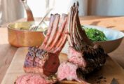 Cutting board with a sliced rack of spring lamb with rosemary, knife, bowl of salad