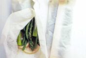 Two packets of steamed vegetables in parchment --asparagus and green beans--on a white plate