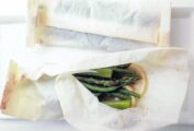 Two packets of steamed vegetables in parchment --asparagus and green beans--on a white plate