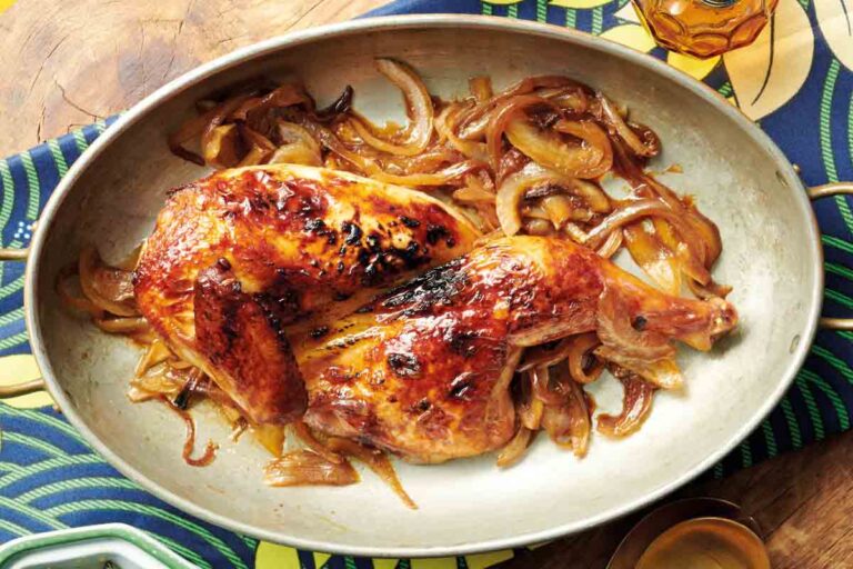 An oval platter filled with pieces of stout and soy roasted chicken on top of caramelized onions.