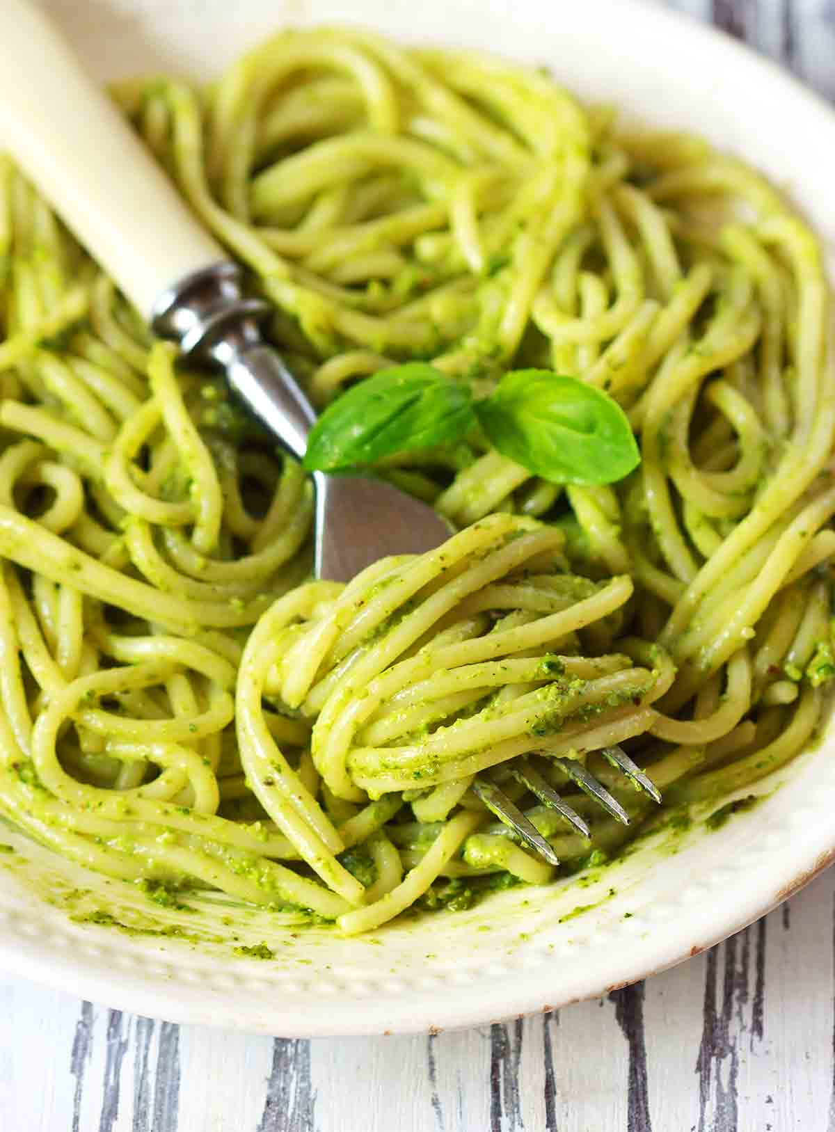 A bowl of pasta tossed with pesto with a fork resting in it
