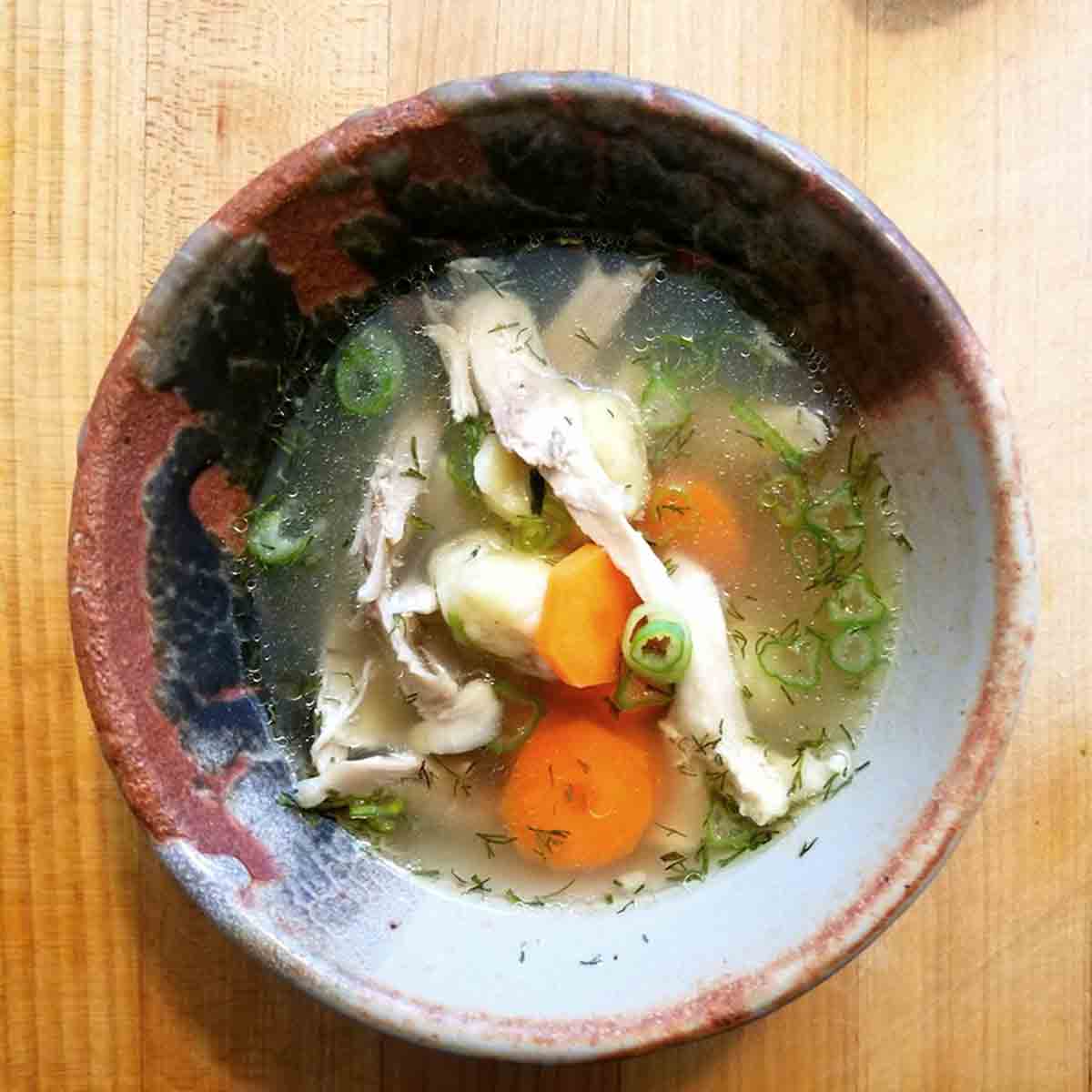 A bowl of Ukrainian chicken dumpling soup with shredded chicken, carrots, scallions, and dill