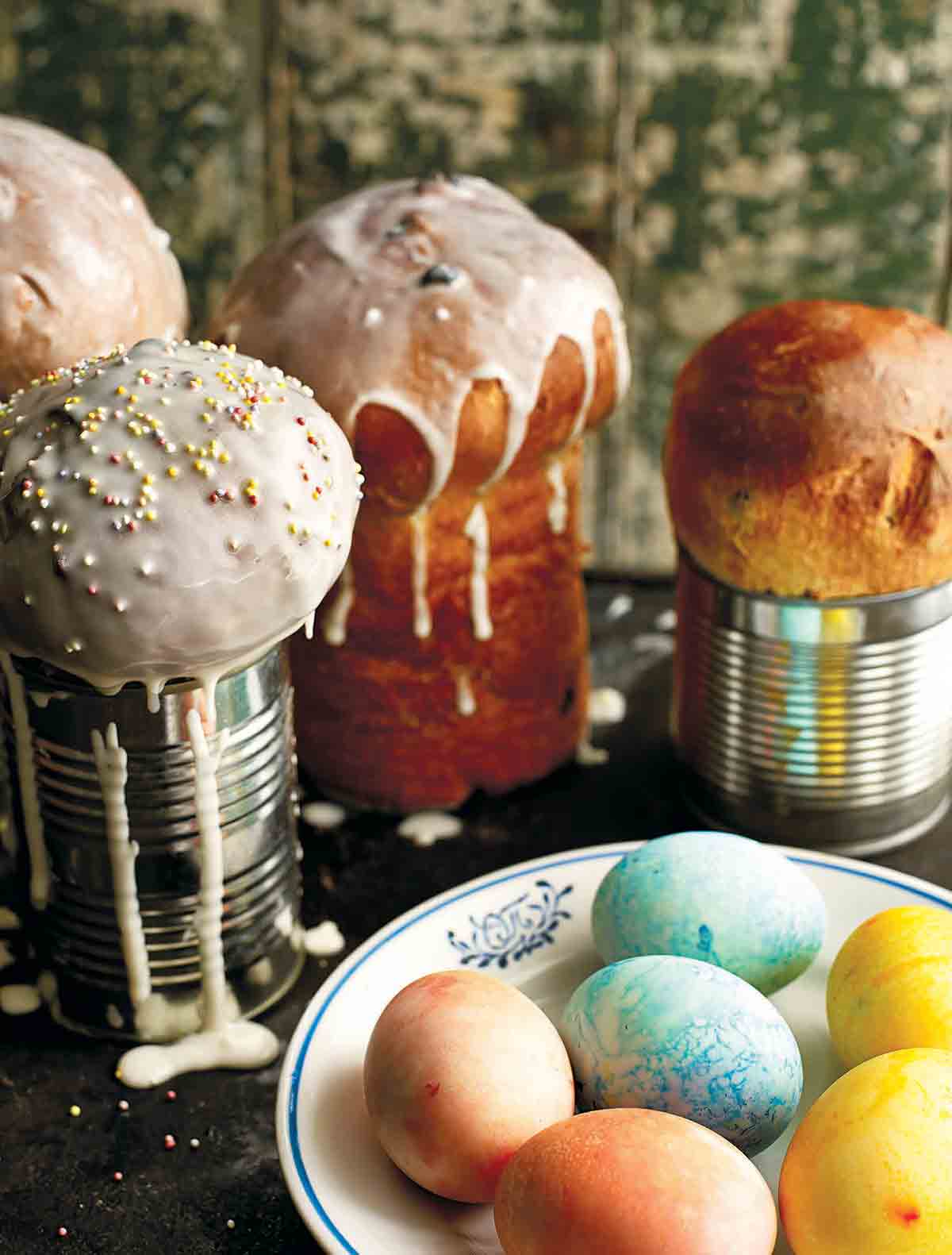 Fyra limpor ukrainskt påskbröd, paska, med en skål med färgade ägg framför sig