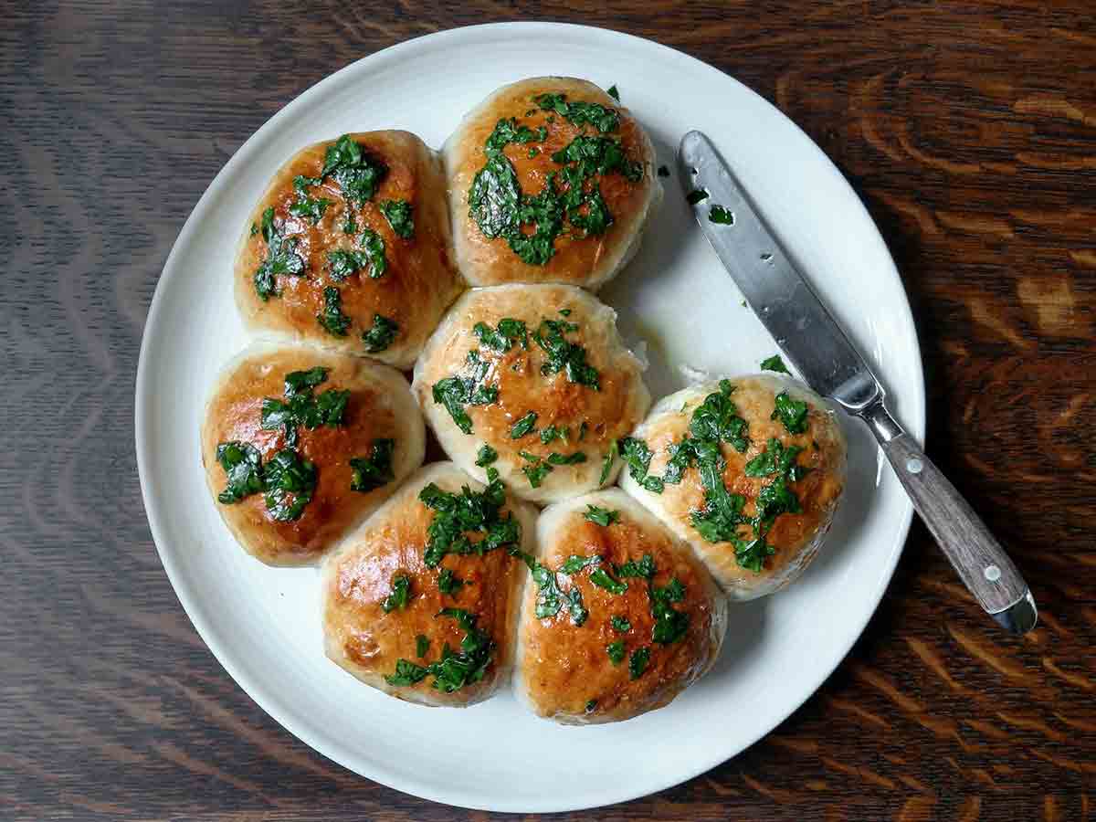 Seven Ukrainian garlic bread rolls on a white plate with a knife on the side