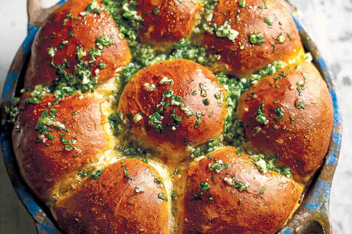A round dish filled with Ukrainian garlic bread rolls, topped with garlic-parsley oil